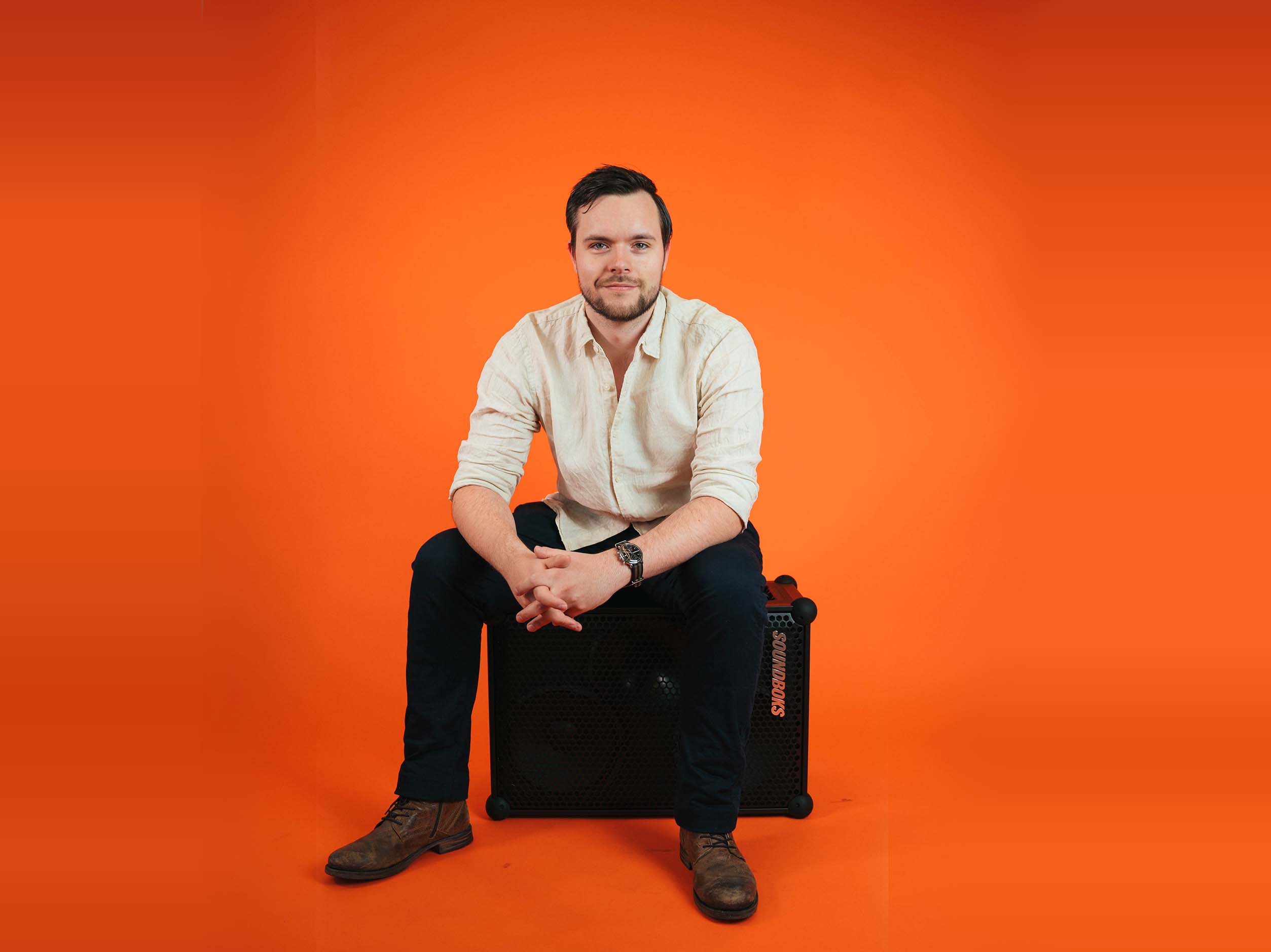 Rene sitting on a SOUNDBOKS in front of an orange background