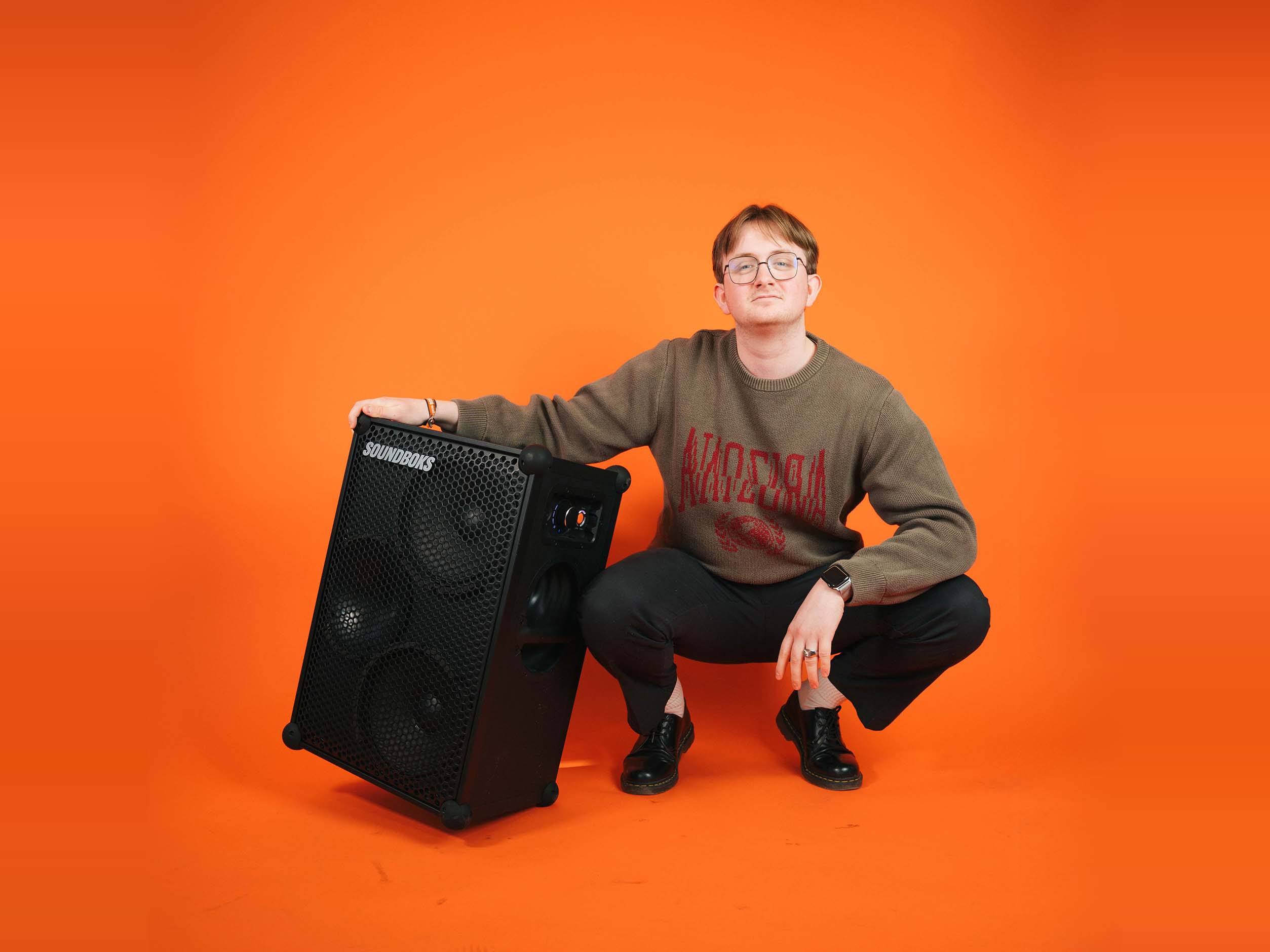 Rasmus sitting with a SOUNDBOKS in front of an orange background