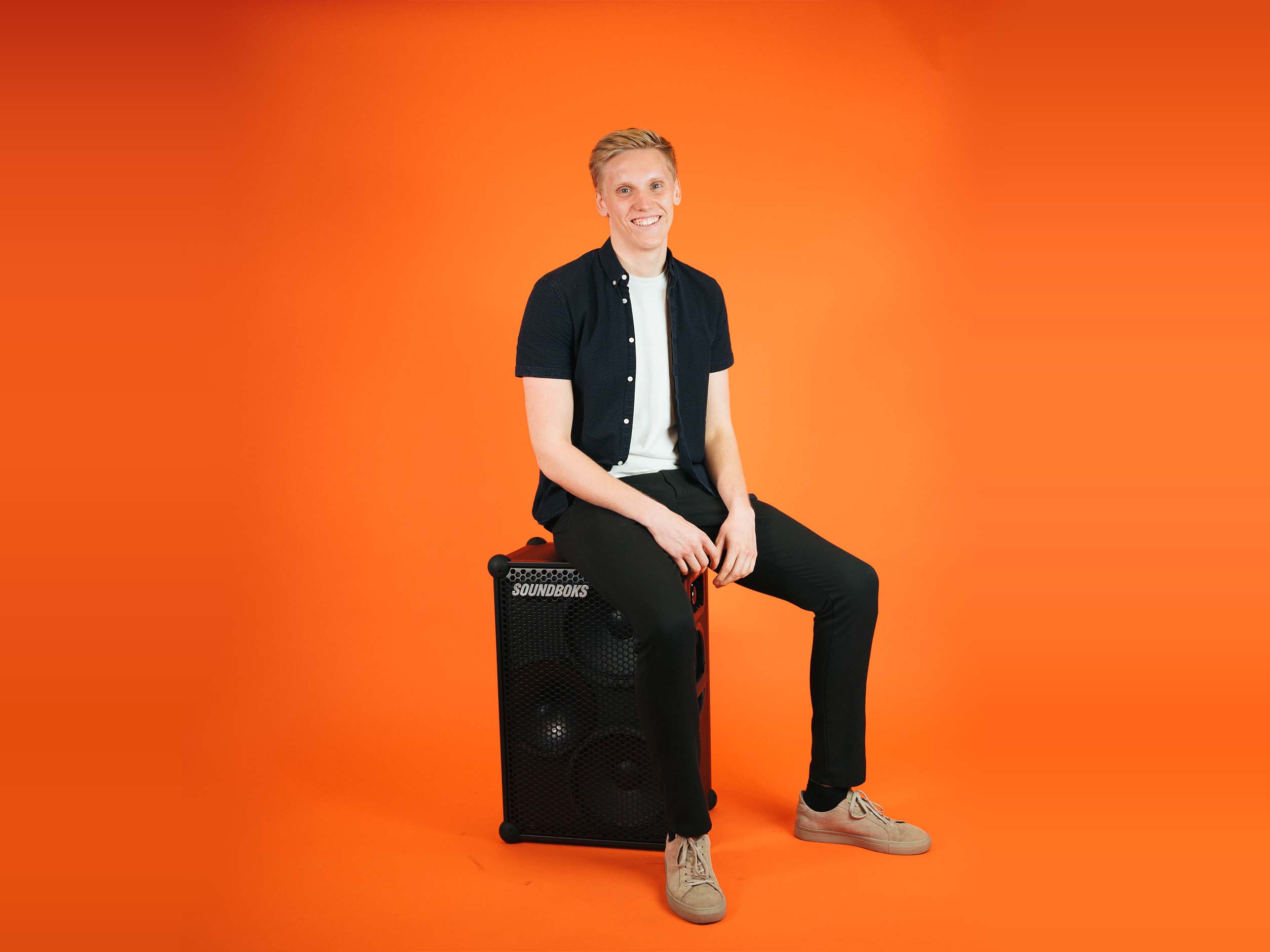 Sebastian soundboks employee, sitting with a SOUNDBOKS in front of an orange background