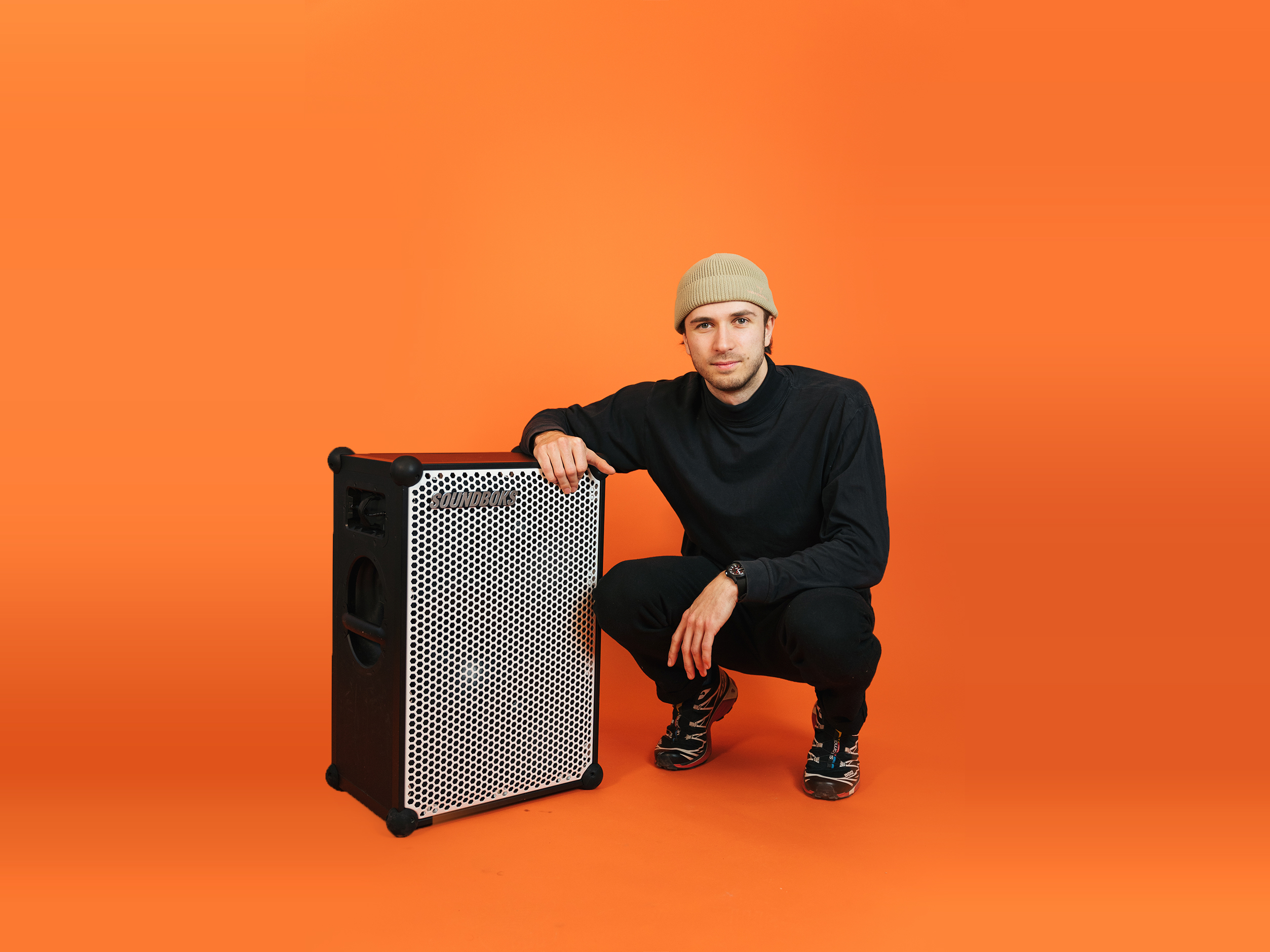 Alfred sitting next to a SOUNDBOKS in front of an orange background