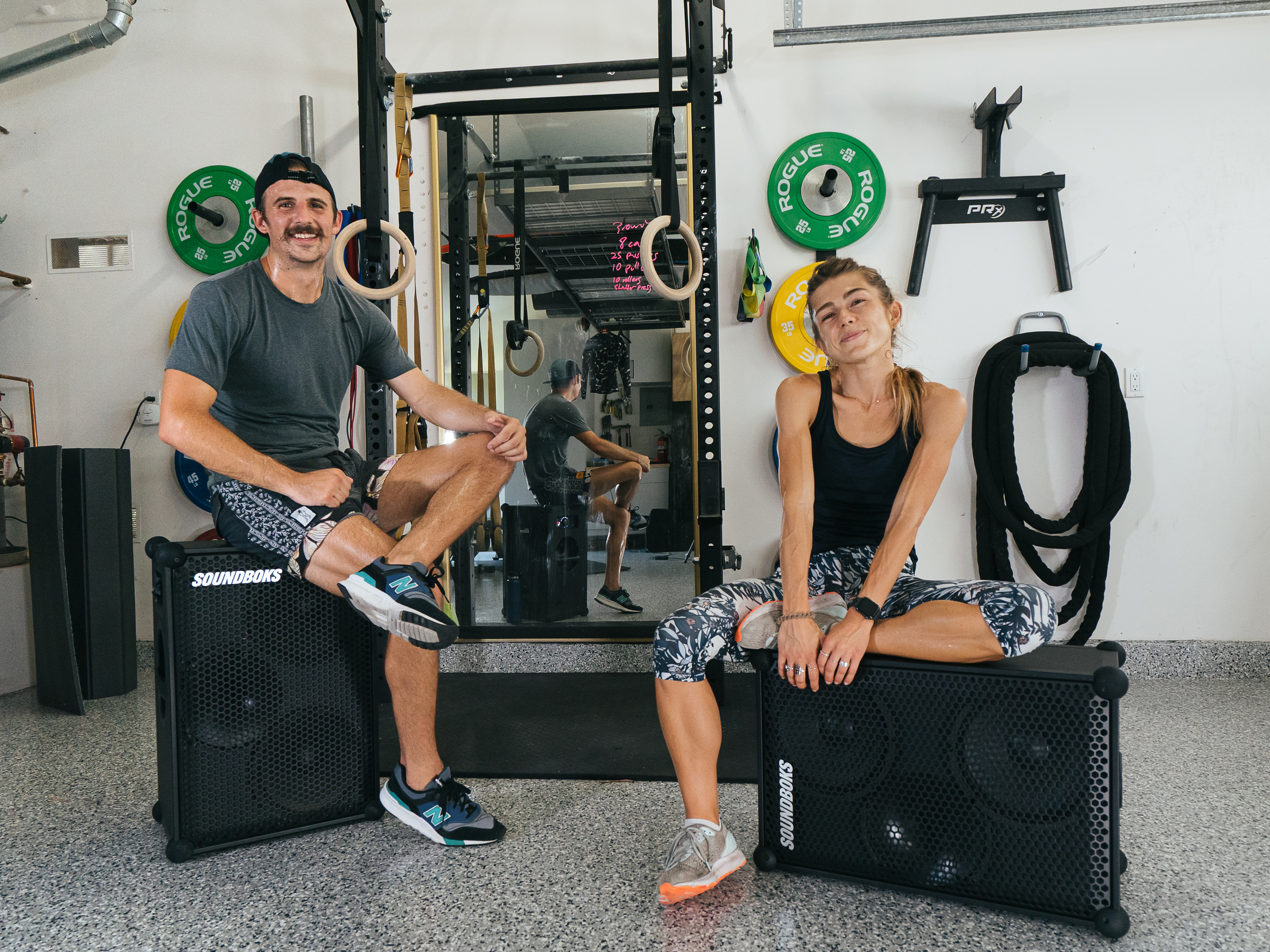 Girl and guy sitting on top of the SOUNDBOKS in a home gym