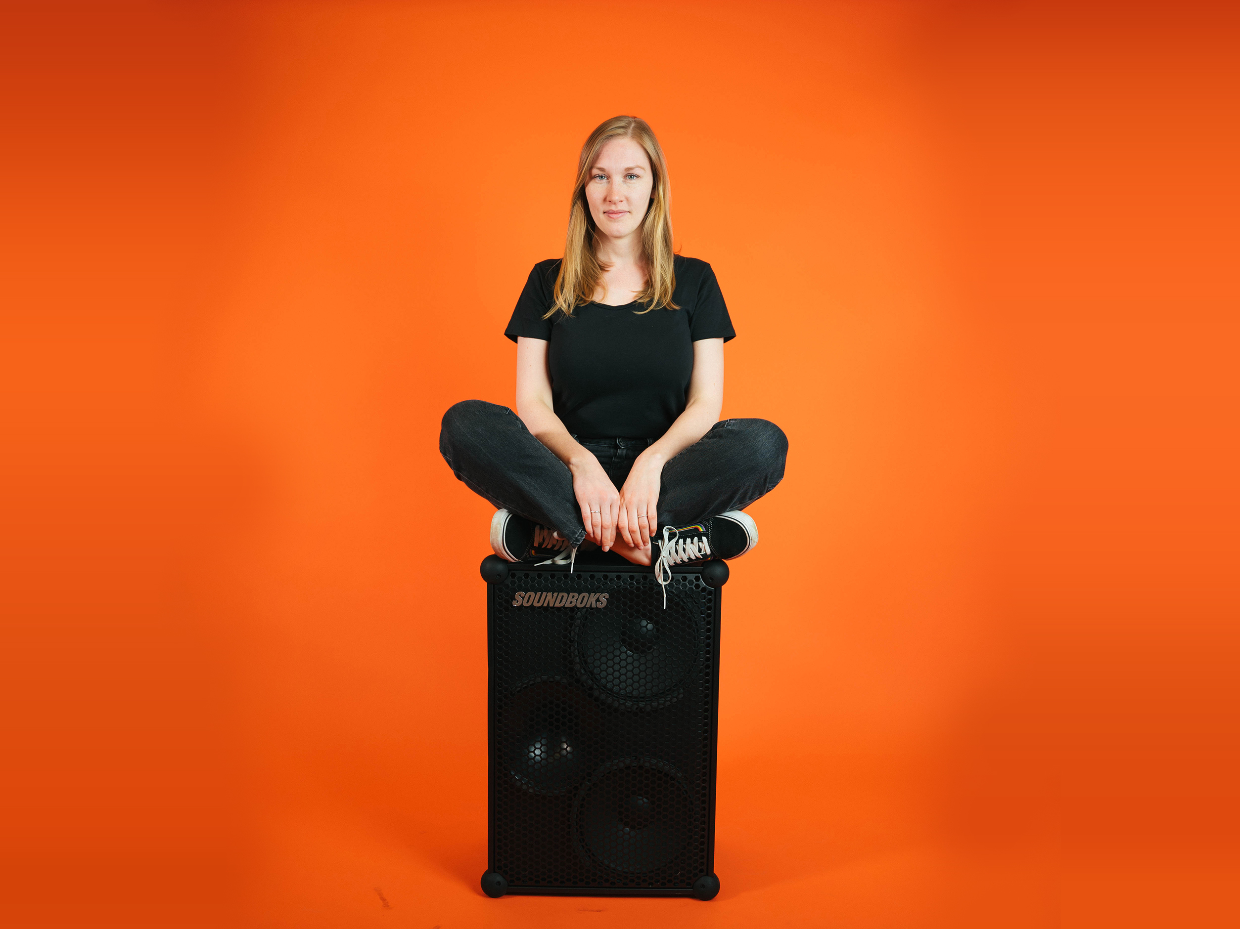 Michelle, a soundboks employee sitting on top of a soundboks in front of an orange background