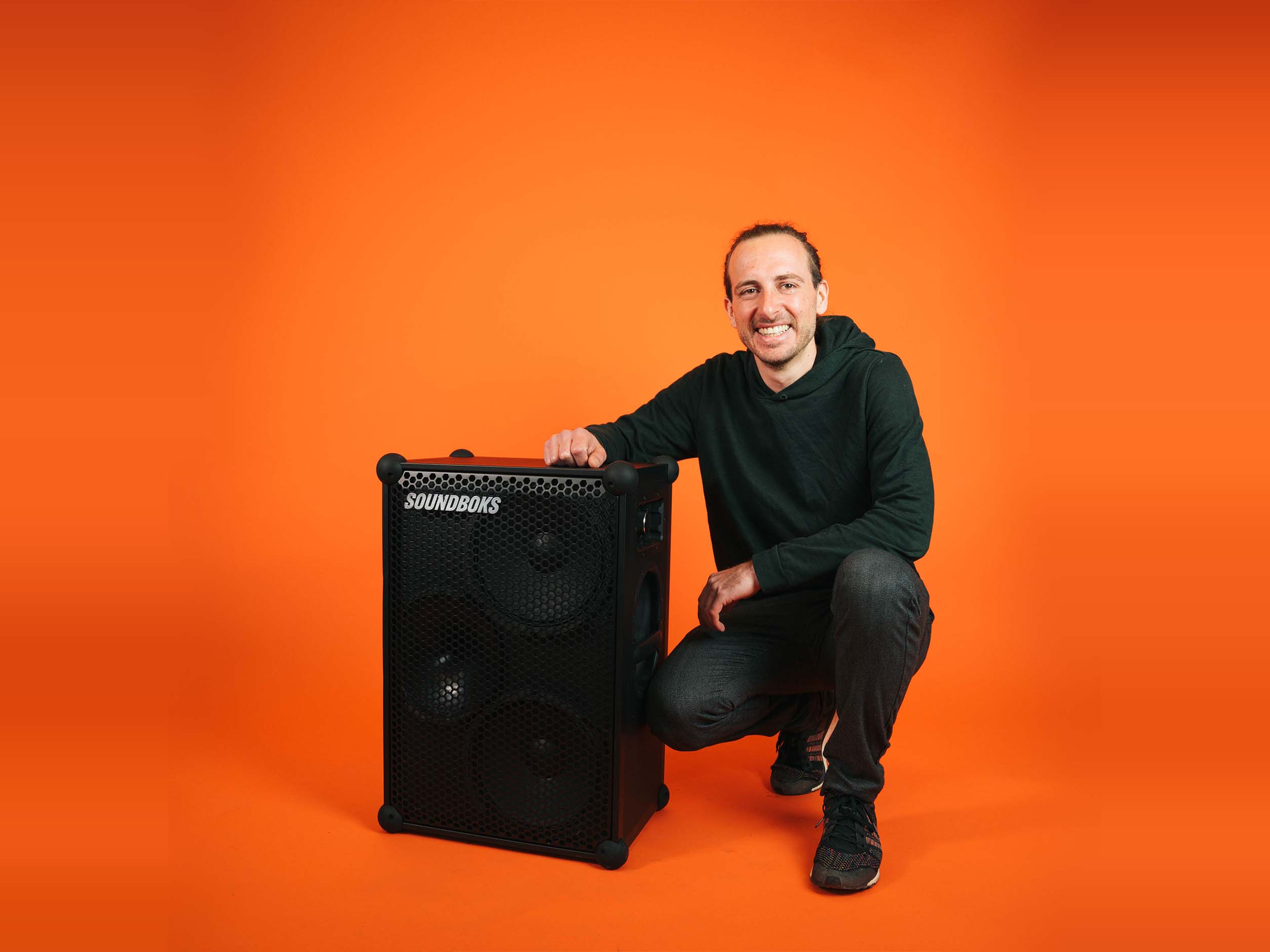 Stephan soundboks employee, sitting with a SOUNDBOKS in front of an orange background