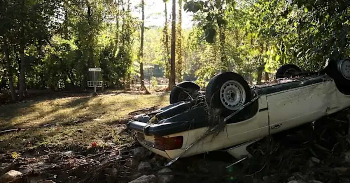 A car flipped over in a rural area near a disc golf basket