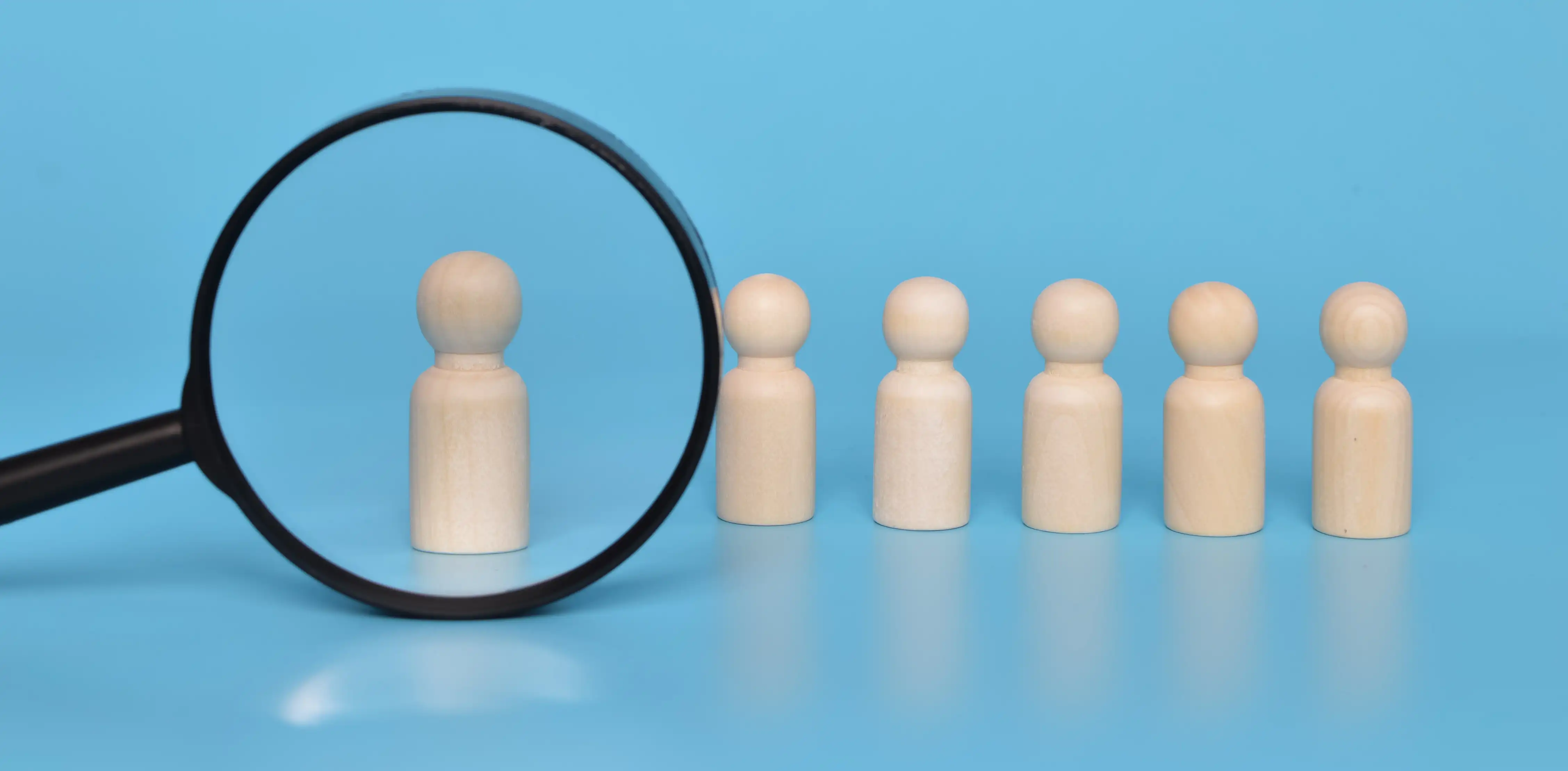 Magnifying glass over wooden figures representing ESG-compliant global talent sourcing