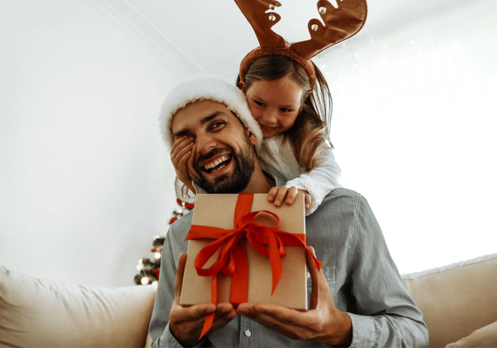 A father and daughter smile and hold a present after overcoming a holiday financial challenge.