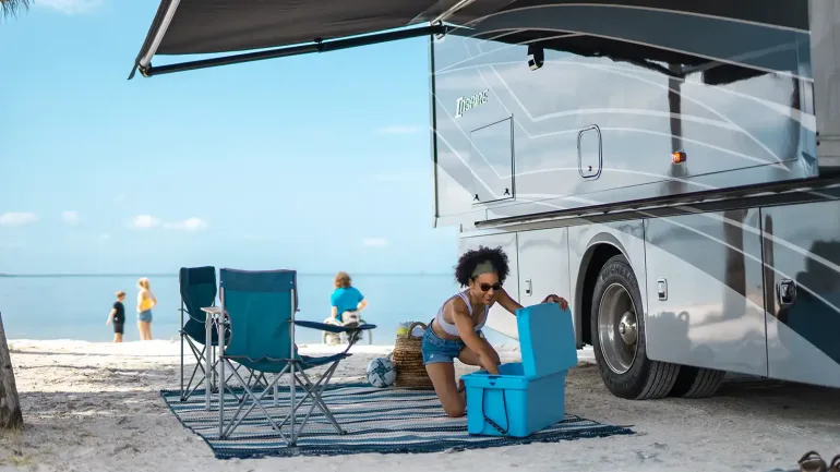 Woman getting drink out of cooler outside of RV that's parked at beach