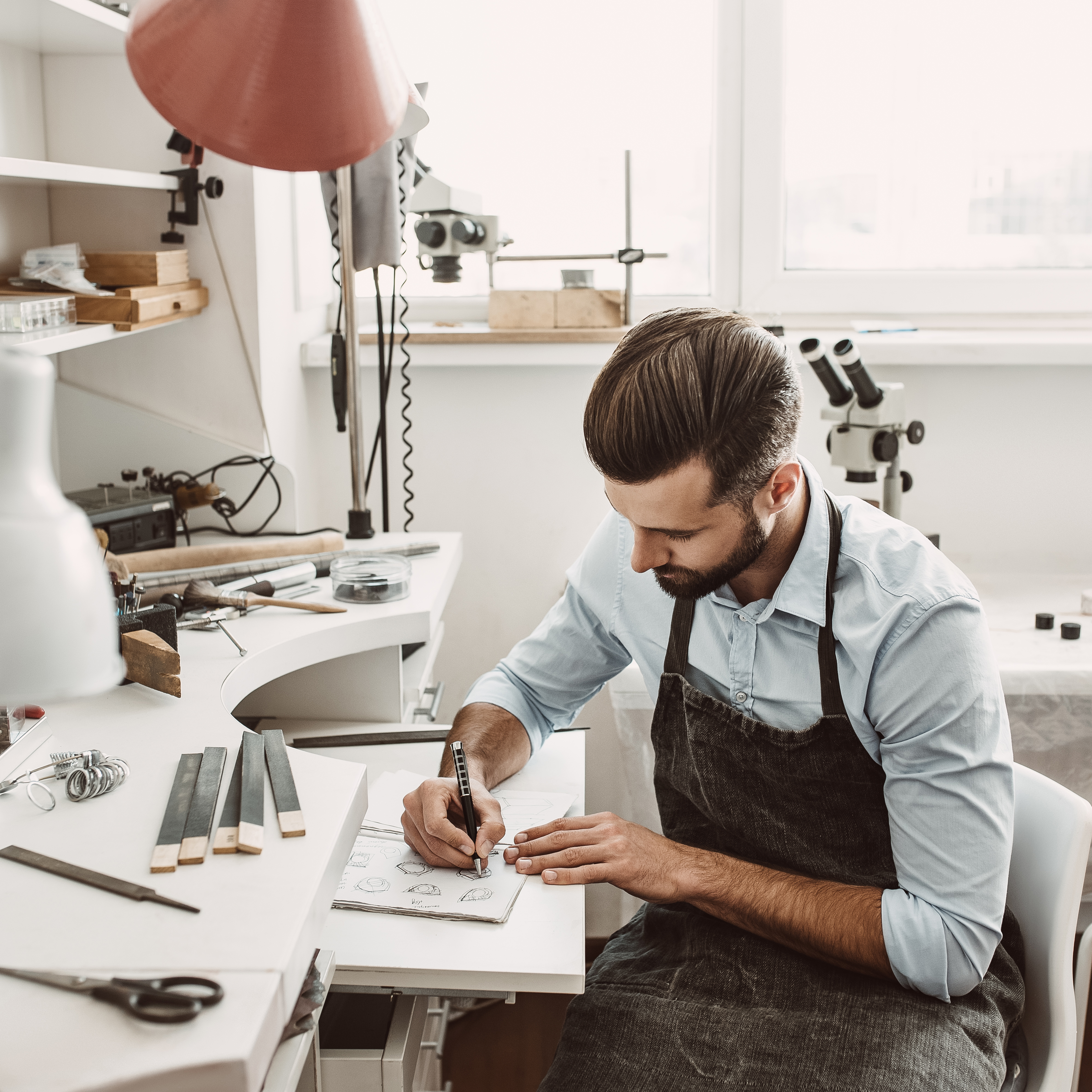 male jeweler sitting at a bench sketching