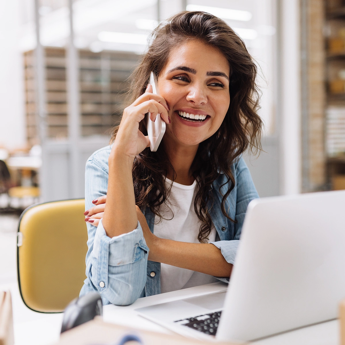 Smiling young woman talking on the phone while sitting at a desk with a laptop