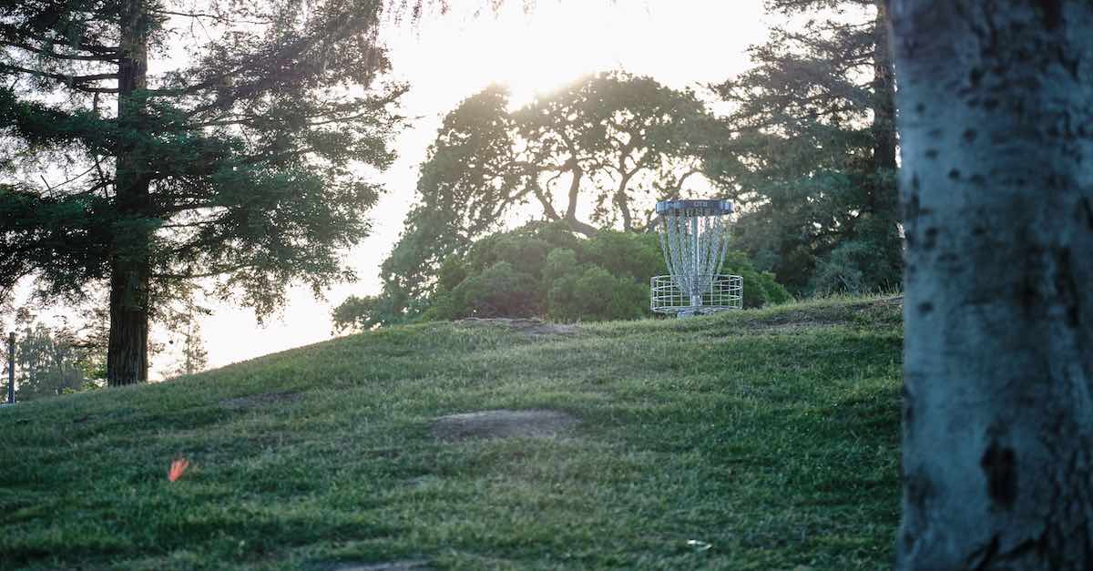 A disc golf basket and sunlight peek over a grassy hill