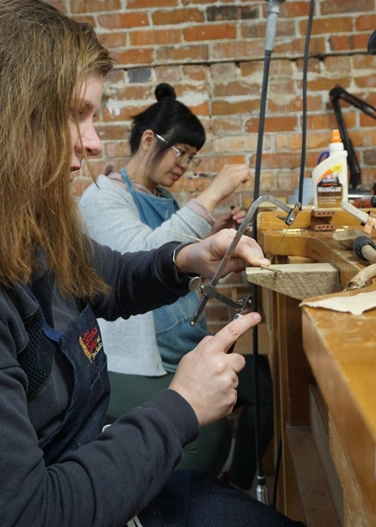 two jewelers sitting at the bench sawing
