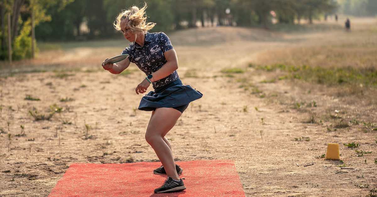 A woman in the middle of throwing a disc, hair and skirt flowing as she spins
