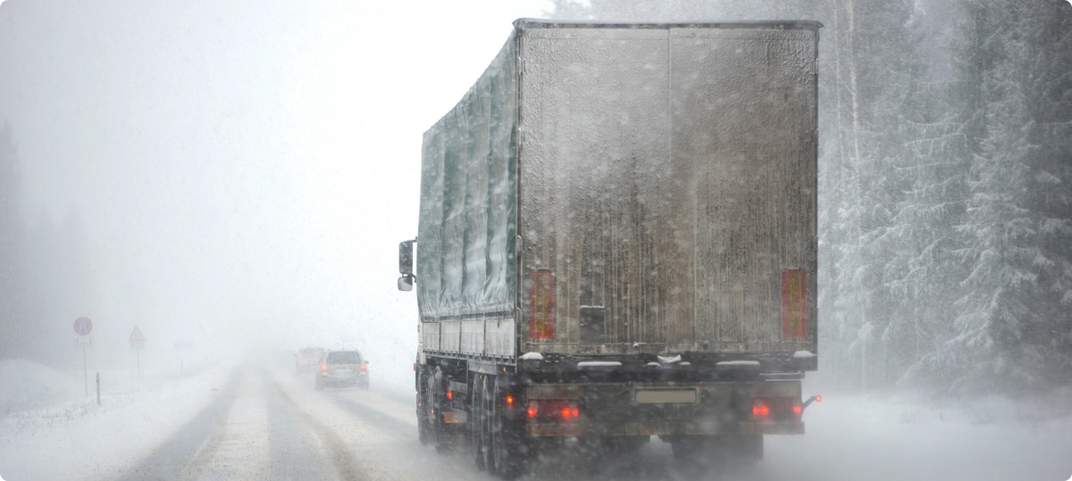 Rear view of a semi truck trailer driving through a winter snow storm on a snowy road