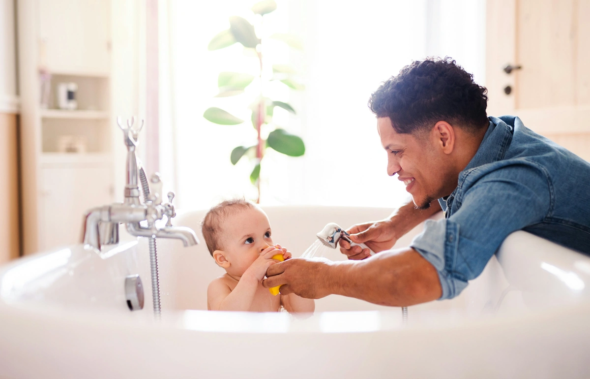 A dad bathing his young baby in a bathtub. 