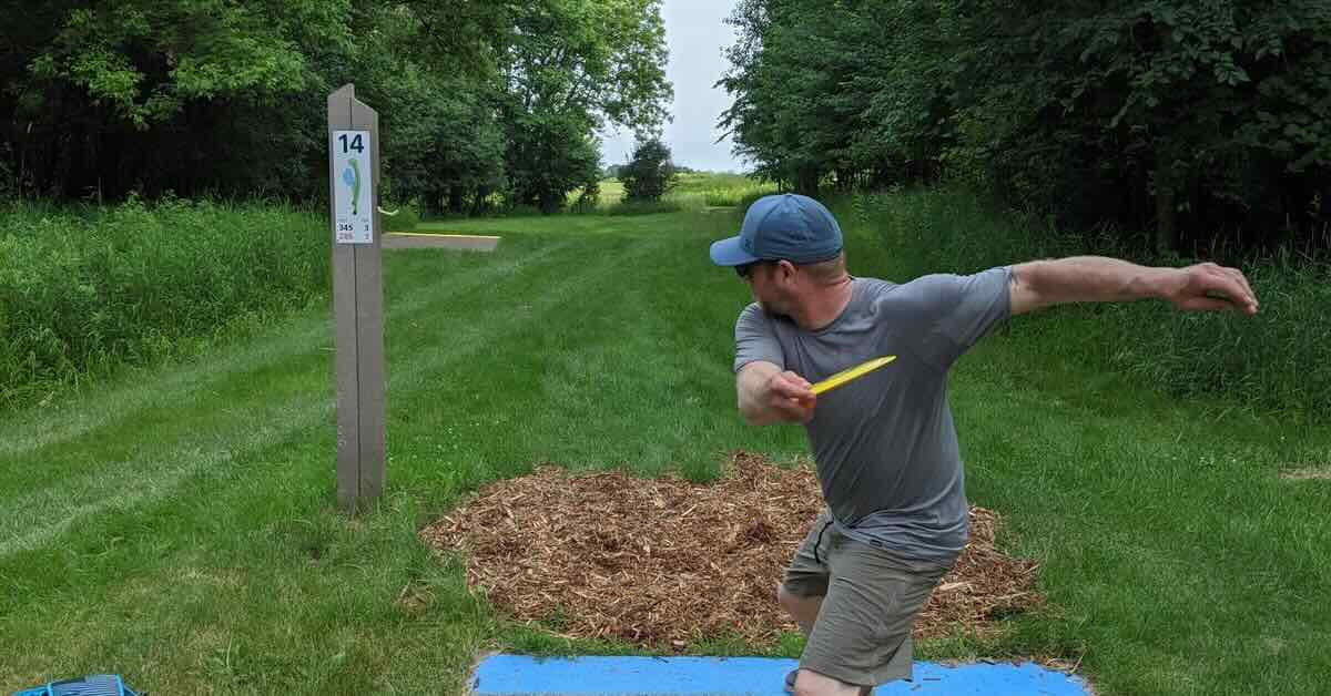 Man in a baseball cap, shorts, and t-shirt throwing a disc golf disc