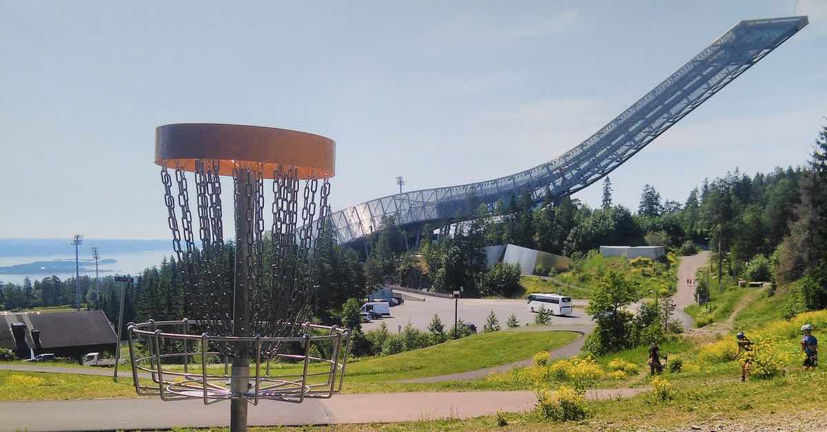 A disc golf basket with a giant ski jump in the background