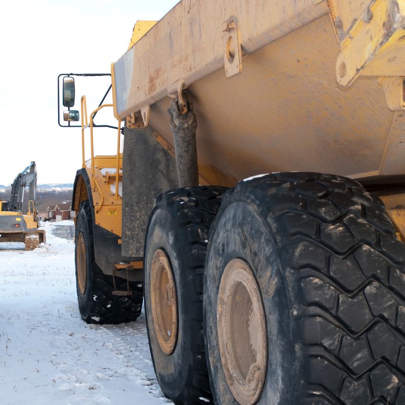 A yellow articulating dump truck and yellow excavator on a snow covered lot