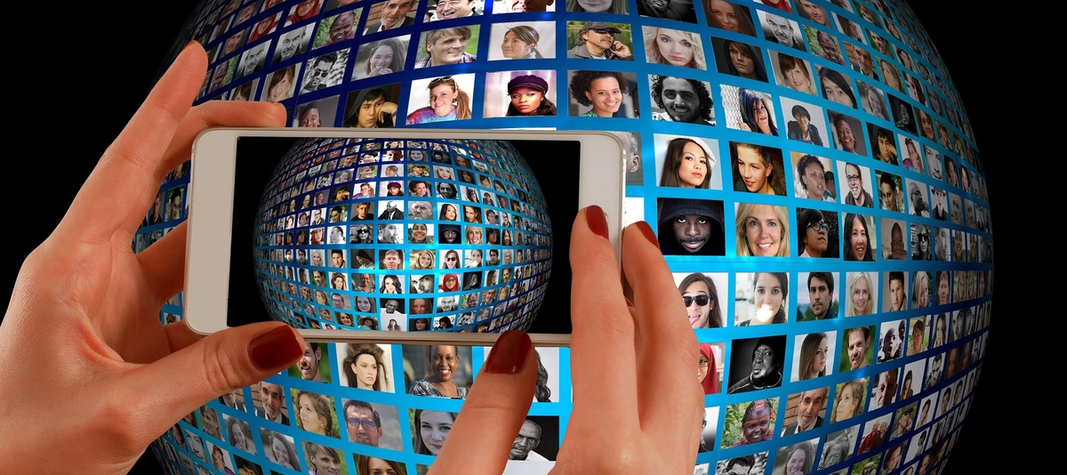 Feminine hands holding a smartphone take a picture of a globe covered with photographs of people's faces.