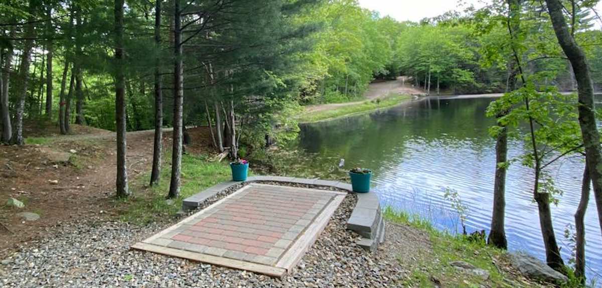 A paver disc golf tee leads to a water carry over a pond