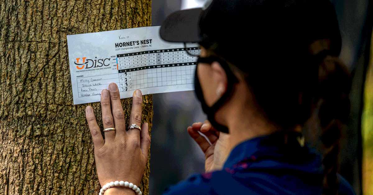 A woman writes on a paper scorecard on a tree