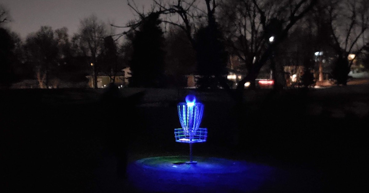 A basket lit up in blue at night with a suburban neighborhood behind