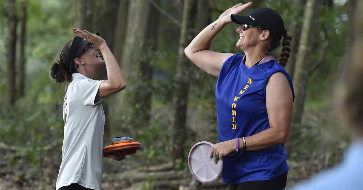 Two women about to high five on a disc golf course
