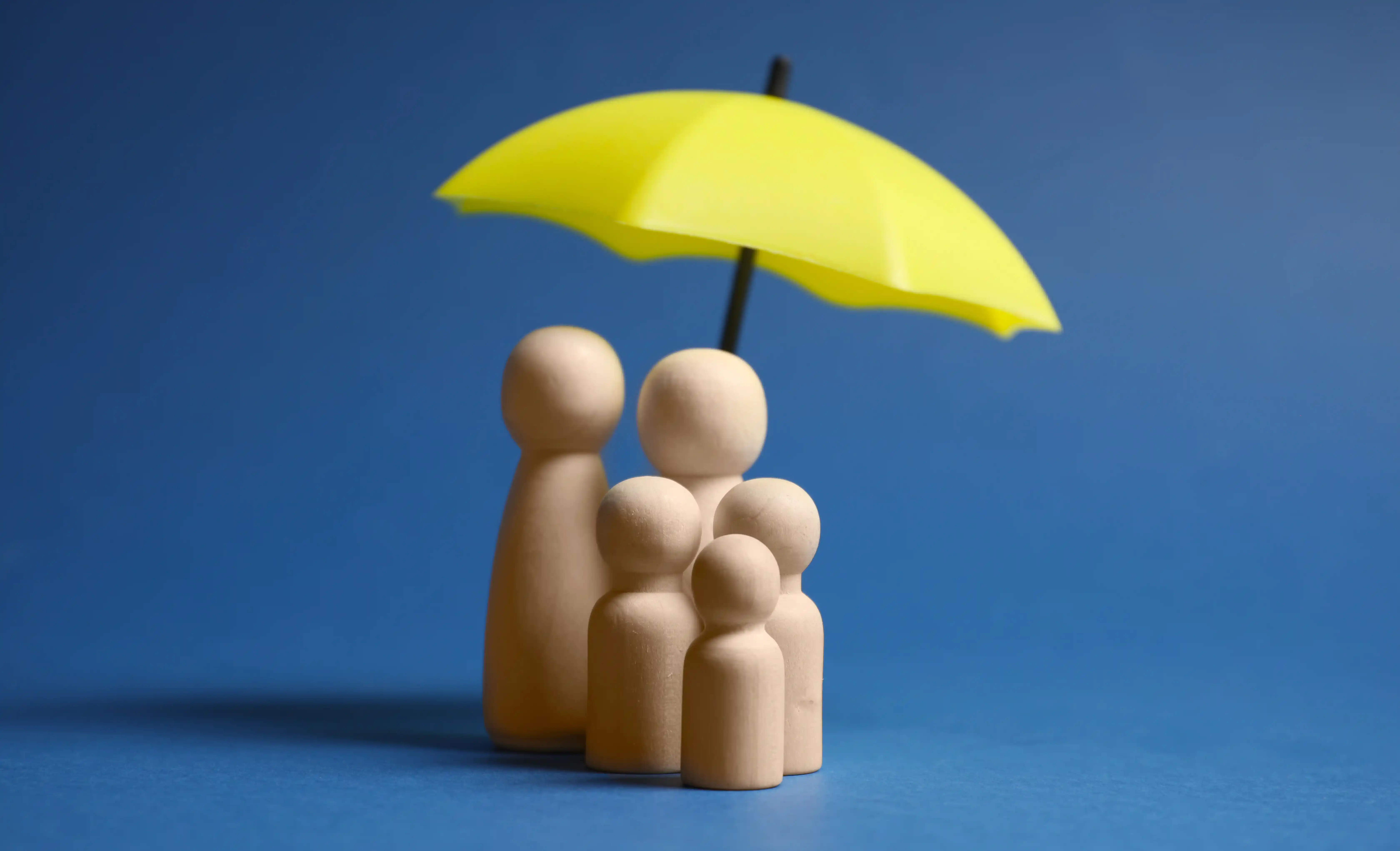 Wooden figures under umbrella representing worker protection and social ESG compliance