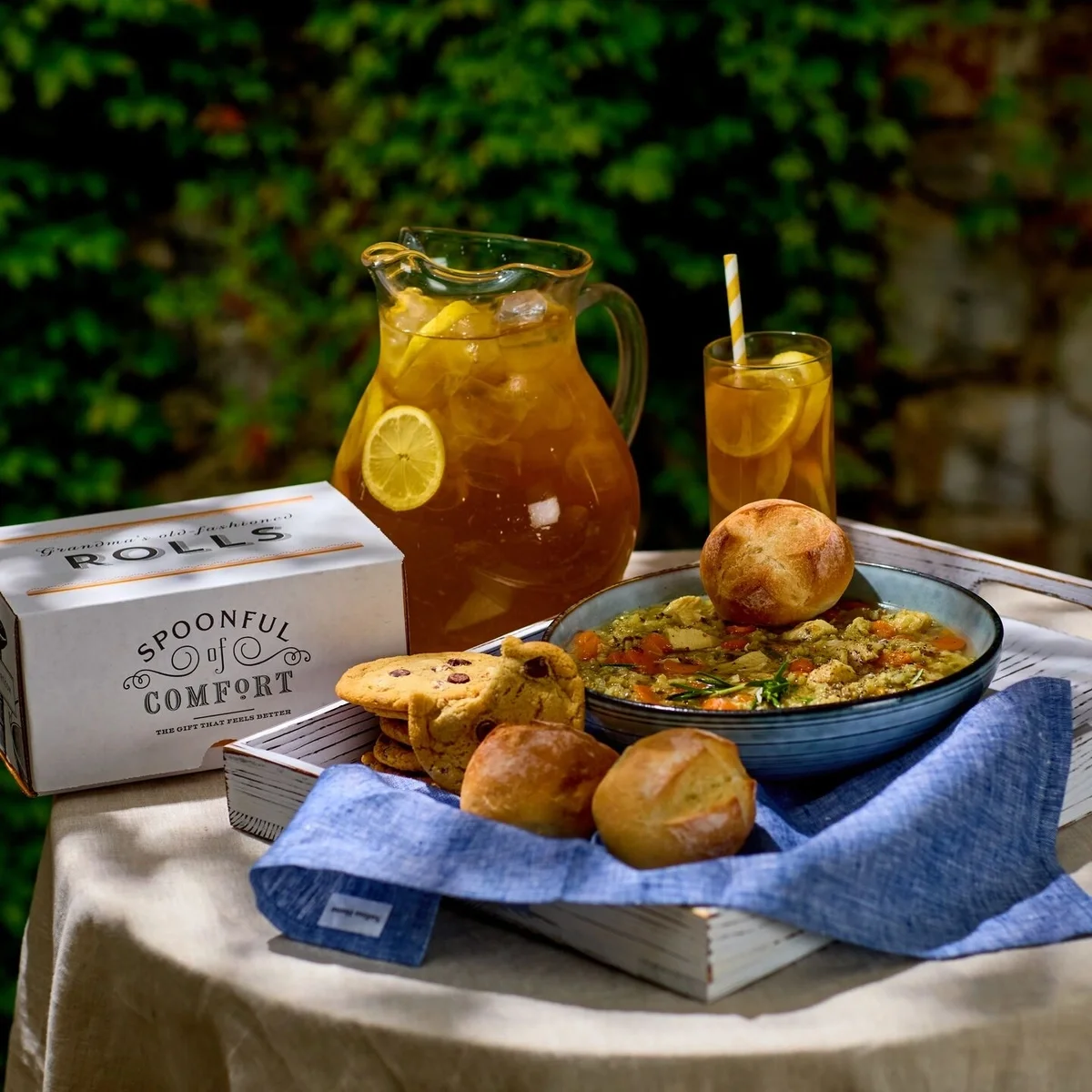 Styled image of a sweet tea pitcher, box of rolls and assorted soups