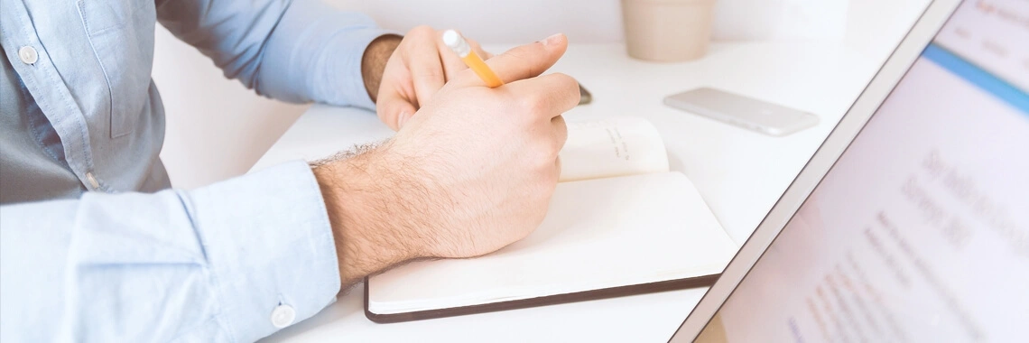 Man at computer writing in his book.