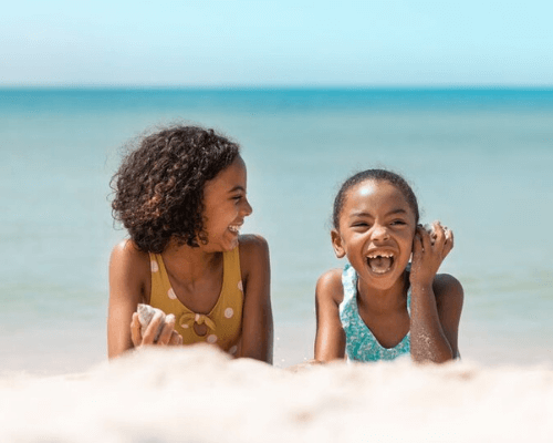 Two children smiling at the beach with ocean background