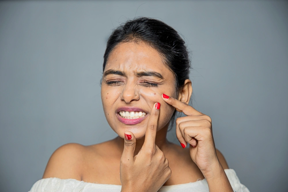 Woman cringing while popping a pimple