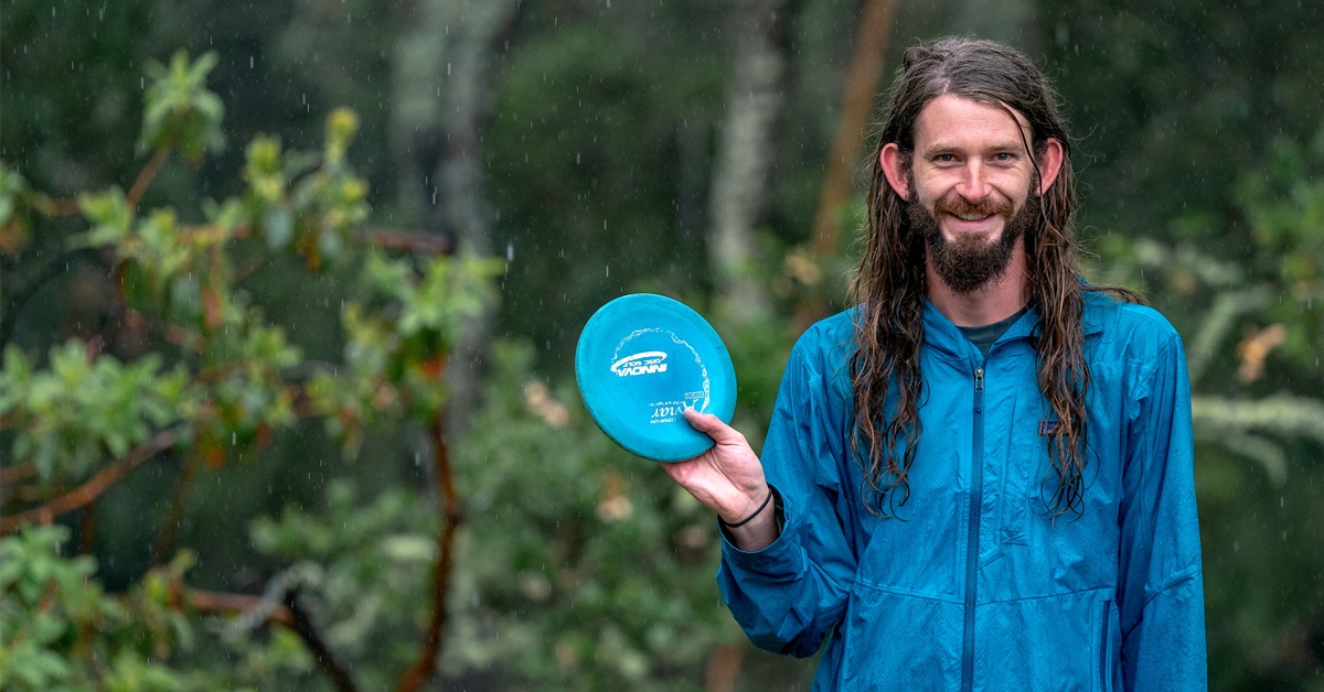 A long-haired man stands in the rain holding a disc