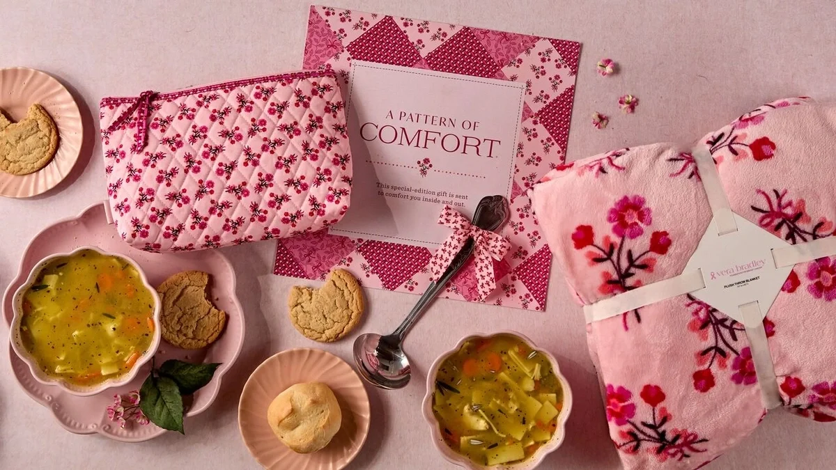 Overhead view of a pink-themed comfort gift featuring two bowls of soup, cookies, a floral throw blanket, matching floral pouch, metal ladle tied with a pink ribbon, and a card that reads “A Pattern of Comfort.”