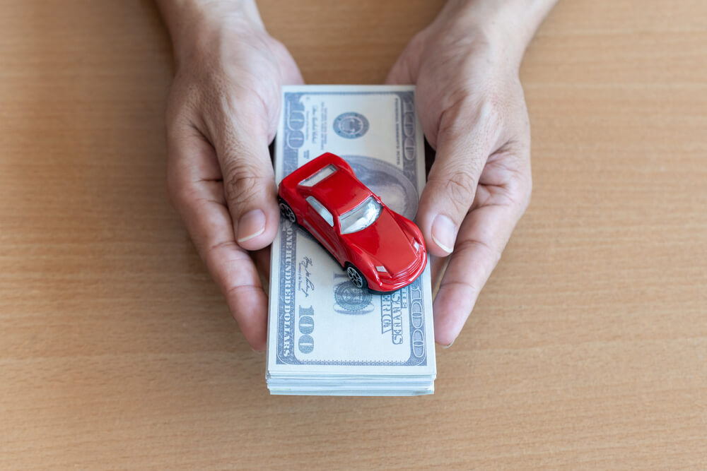 hands holding title cash with toy car on top