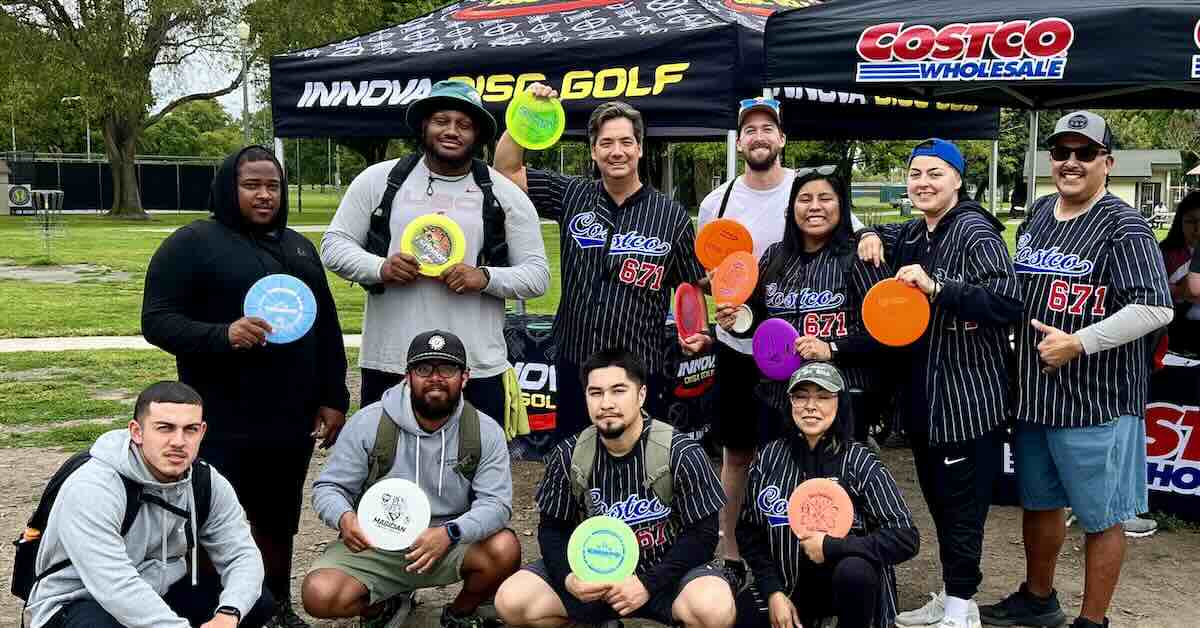 A group poses with discs for a group photo in front of Innova and Costco tents