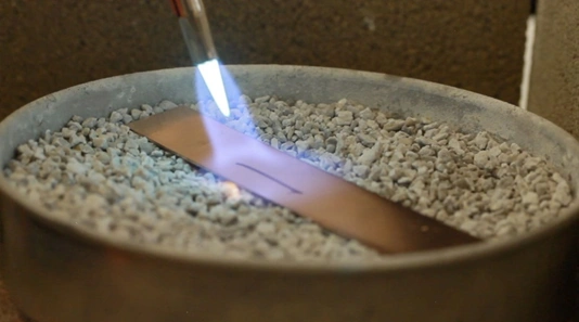 Jewelry torch annealing a piece of copper in a pan with pumice rocks