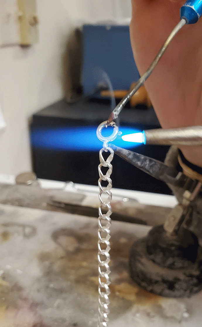 someone soldering a spring ring clasp to a piece of chain