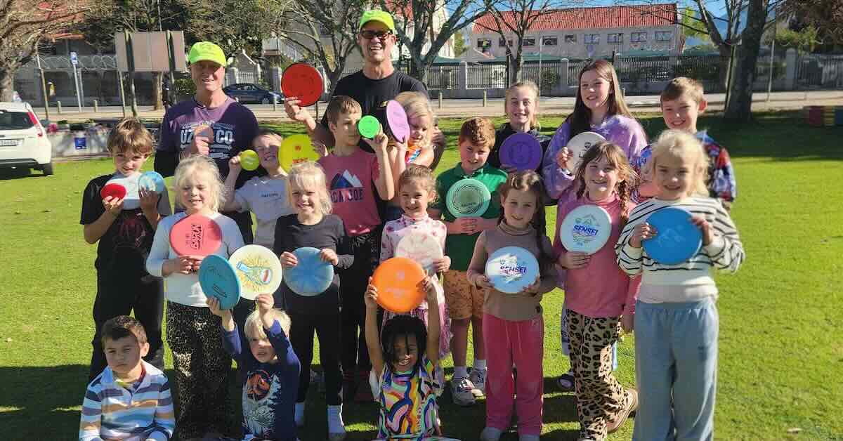 Group of kids and a couple of adults posing for a photo with discs in their hands