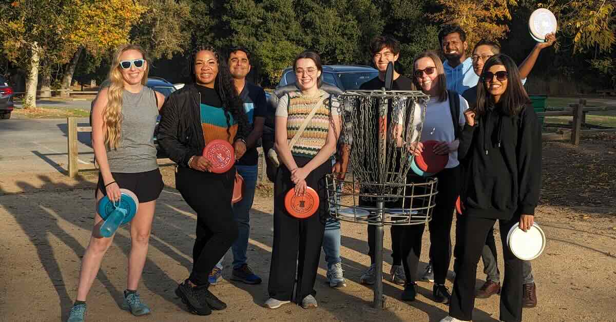 A group of people pose around a disc golf basket