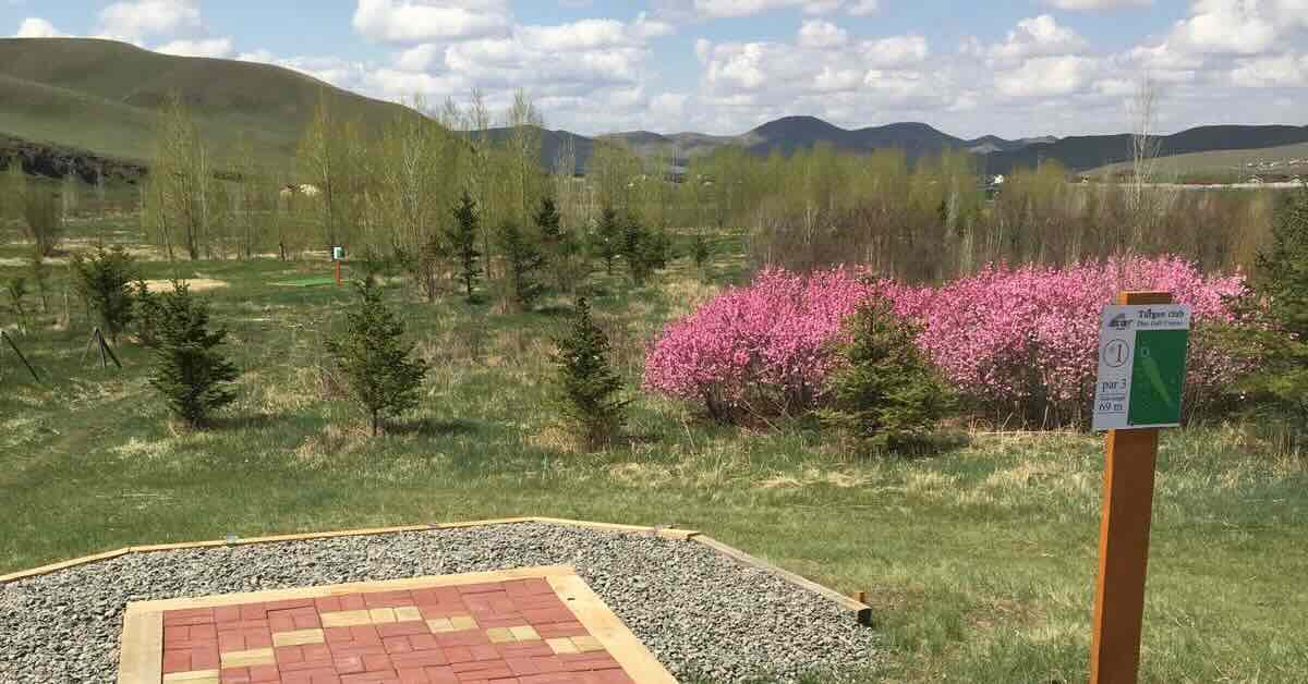 The end of a disc golf tee pad and a tee sign in an open field with mountains beyond