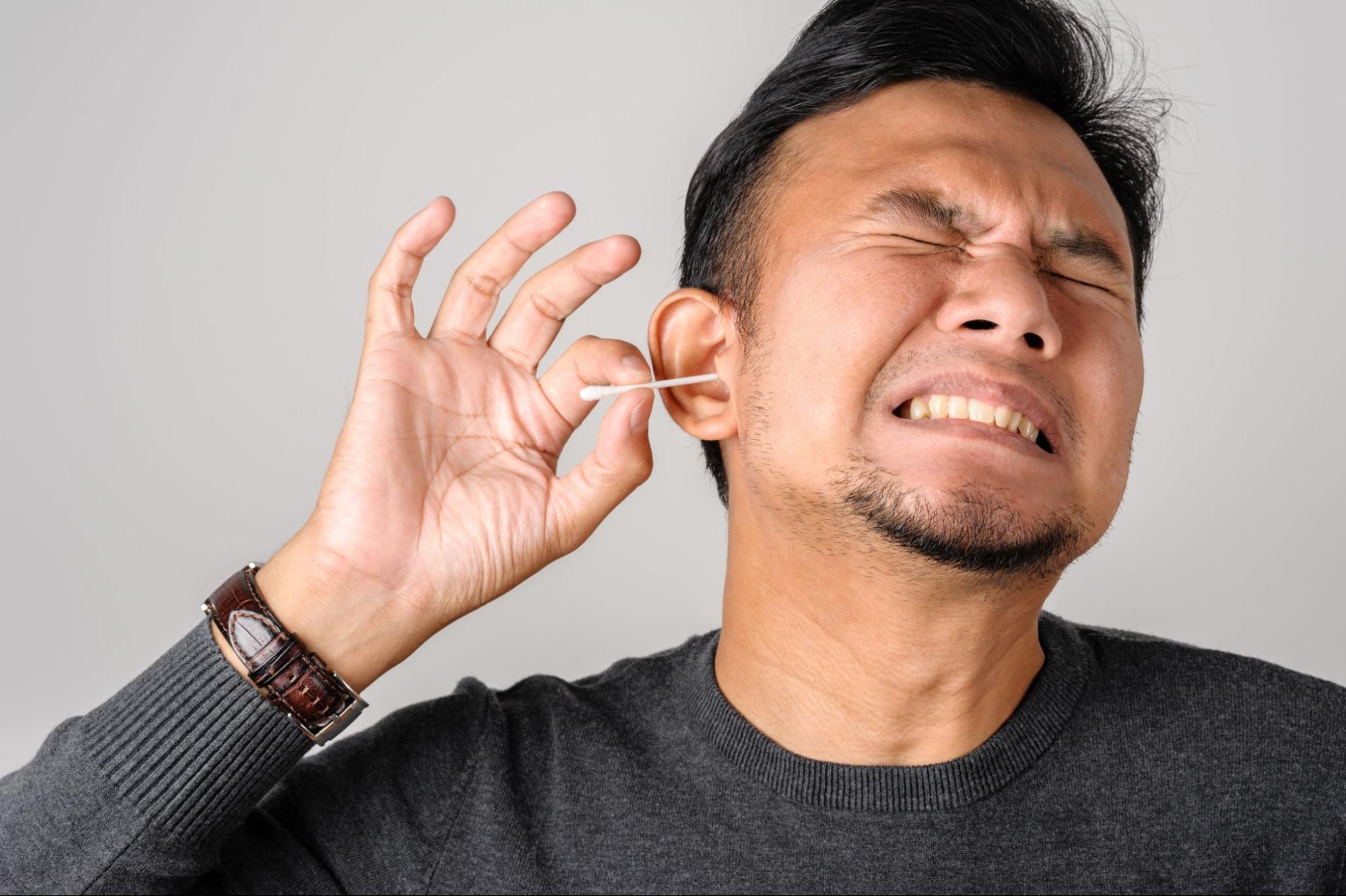 how to get water out of your ear: Man cleaning his ear with a cotton swab