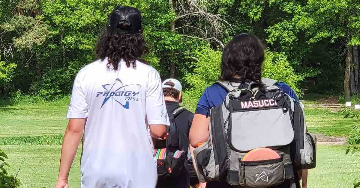 Photo of a young man and older woman from behind, the man holding a disc and the woman carrying a disc golf bag