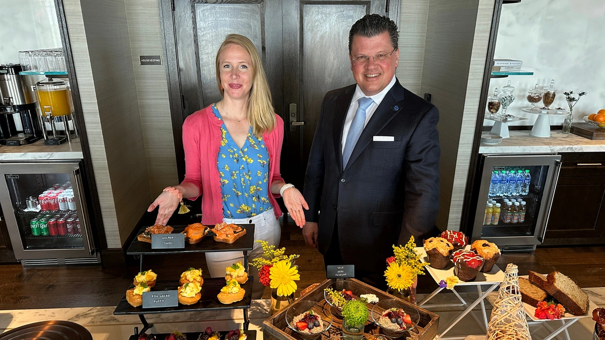 Darley Newman and a man in a suit stand behind a table filled with a variety of appetizers.