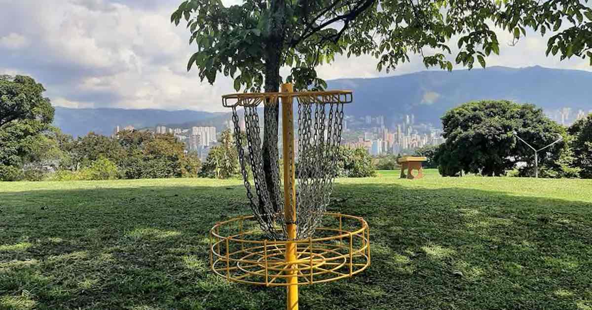 Yellow disc golf basket with mountains and city in the distance