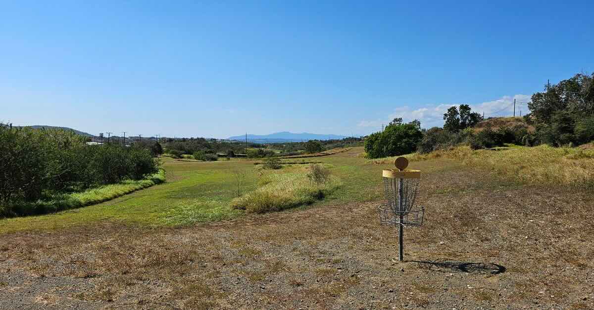 Disc golf basket on a sunny day in a gravelly area and a lawn in the background
