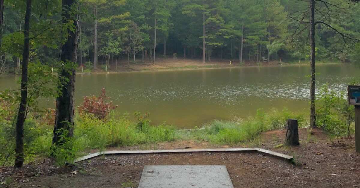 A concrete disc golf tee pad in front of a pond in. wooded area