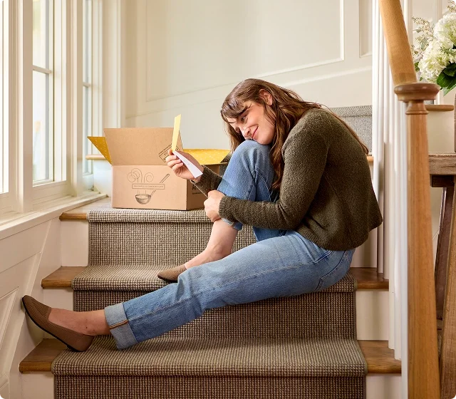 Woman sitting on stairs, reading a heartfelt message and box of Spoonful of Comfort