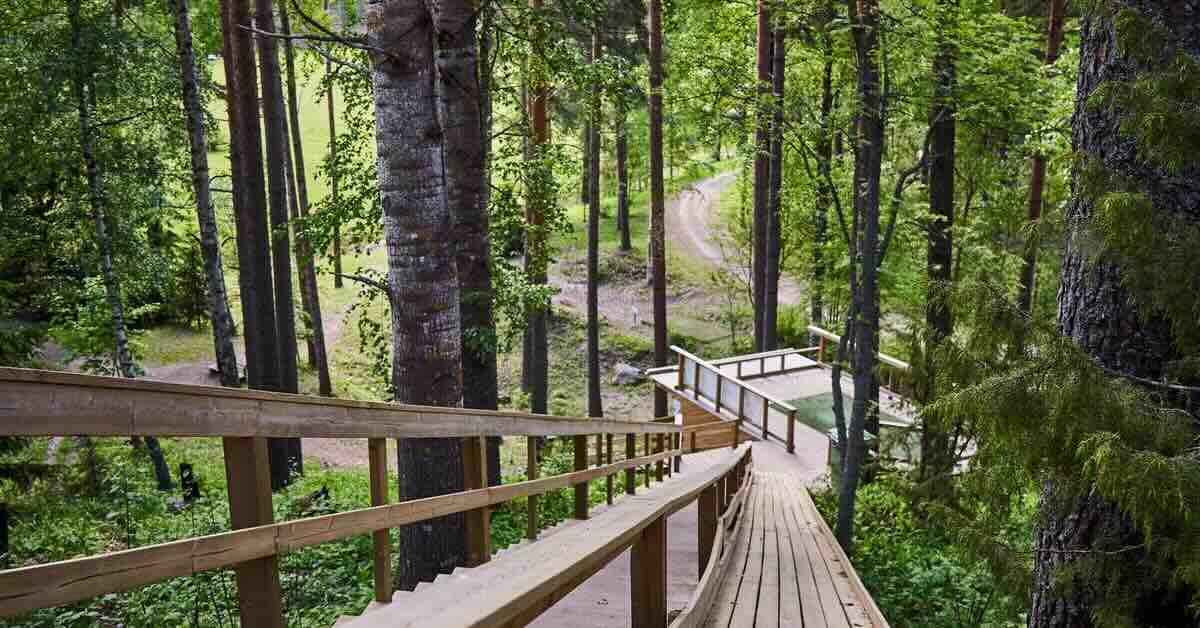 A wooden staircase leads to a wooden platform below with a turf disc golf tee pad