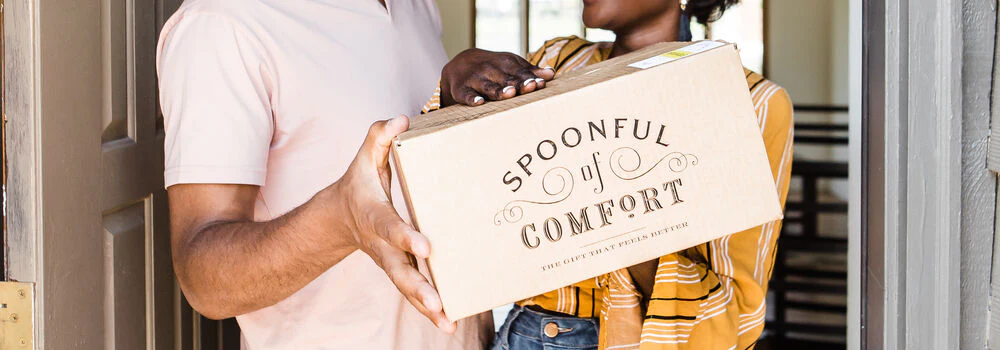 Two people holding in a doorway holding a Spoonful of Comfort care package