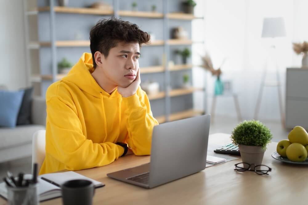 Man in yellow hoodie using a laptop wondering if he can get a loan as he is unemployed